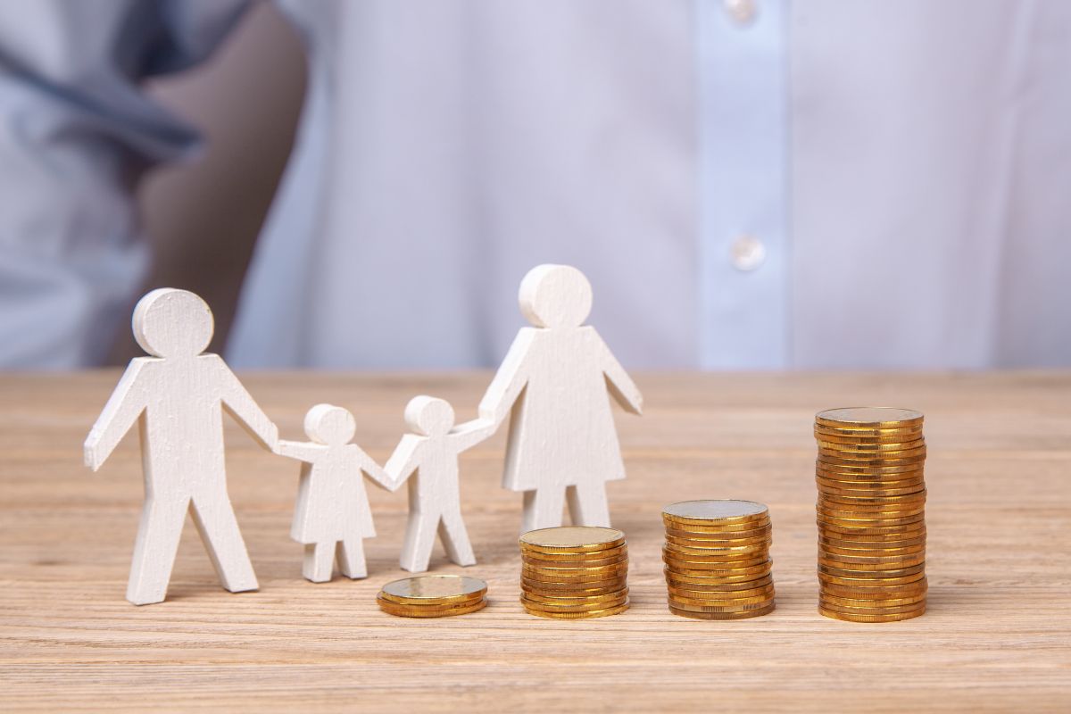 A 3D wooden pictogram family of four standing next to stacks of coins of various quantities